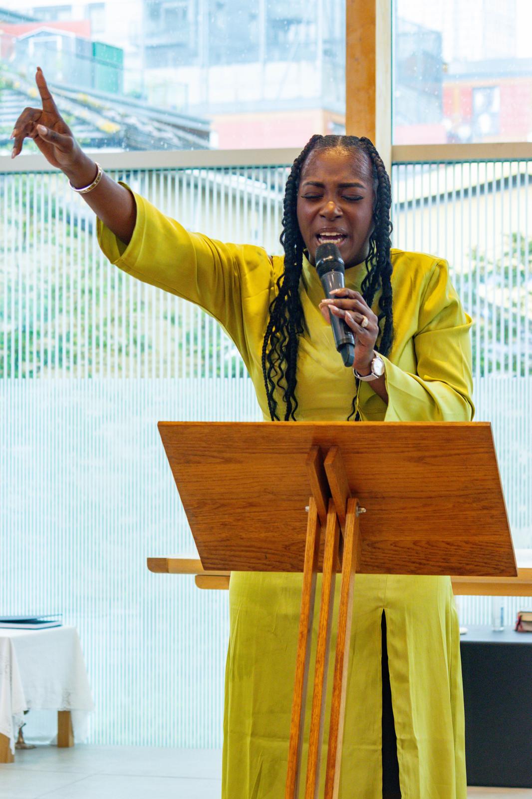 Pastor Nikki Okedele speaking in yellow outfit at TTYM Ministry event